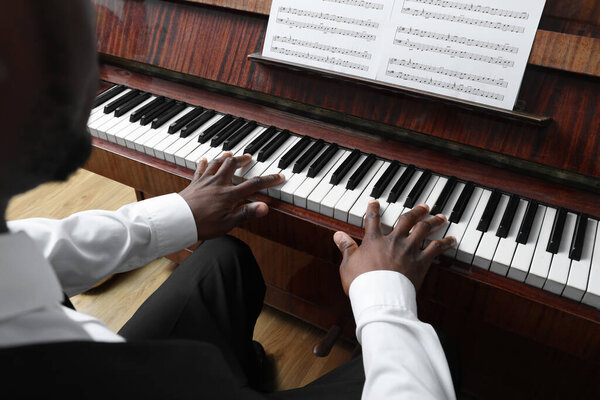 African-American man playing piano indoors, closeup. Talented musician