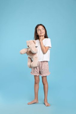 Açık mavi arka planda oyuncak ayıyla pijama giyen hoş bir kız.