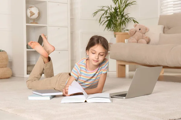 Girl with laptop and books lying on floor at home