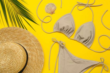 Şık bej bikini, sarı arka planda şapka ve deniz kabuğu.