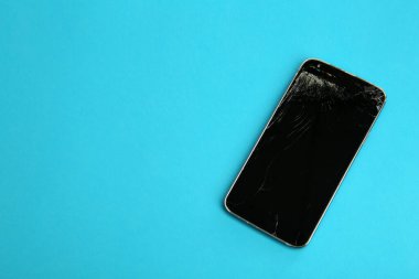 Açık mavi arkaplanda çatlak ekranı olan akıllı telefonun üst görünümü, metin için boşluk. Aygıt onarımı