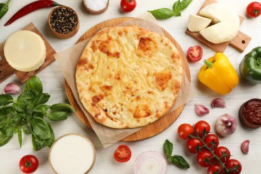 Peynirli lezzetli khachapuri beyaz ahşap masa üzerinde farklı ürünlerle çevrili, düz yatıyordu.