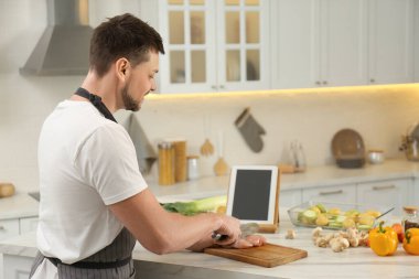 Mutfakta tabletle yemek kursunu izlerken tavuk filetosu kesen adam.