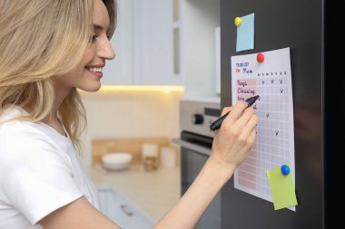 Genç bir kadın mutfaktaki buzdolabı kapısının listesini istiyor.