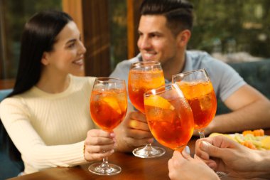 Arkadaşlar masada Aperol spritz kokteyli içiyor, ellere odaklanıyor.