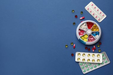 Mavi arka planda farklı haplar içeren plastik kutu, düz. Metin için boşluk