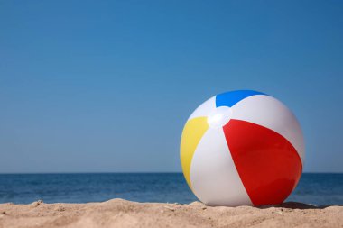 Colorful inflatable ball on sandy beach. Space for text clipart
