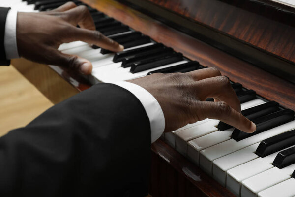 African-American man playing piano indoors, closeup. Talented musician