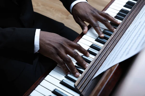 African-American man playing piano indoors, closeup. Talented musician