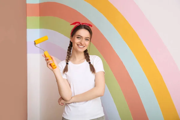 年轻女子在墙边拿着带彩绘彩虹的滚筒 — 图库照片