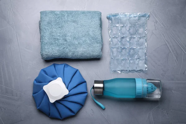 Bottle of water, cold compress, ice pack and towel on grey background, flat lay. Heat stroke treatment