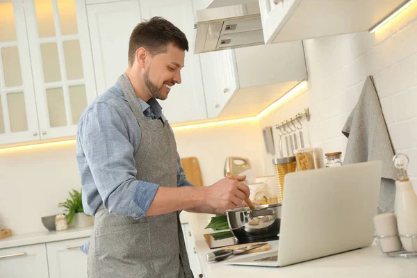 Adam mutfakta dizüstü bilgisayarla yemek pişirirken yemek yapıyor.