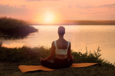 Bir kadın alacakaranlıkta nehrin kenarında meditasyon yapıyor.