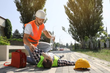 Bir şişe suyu olan bir işçi. Şehir sokaklarında iş arkadaşına yardım ediyor. Sıcak çarpmasından muzdarip.