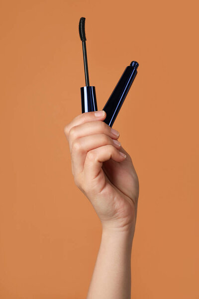 Женщина держит тушь для ресниц на светло-коричневом фоне, крупным планом