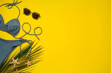 Şık mavi bikini, güneş gözlüğü ve sarı arka planda deniz yıldızları, düz yatak. Metin için boşluk