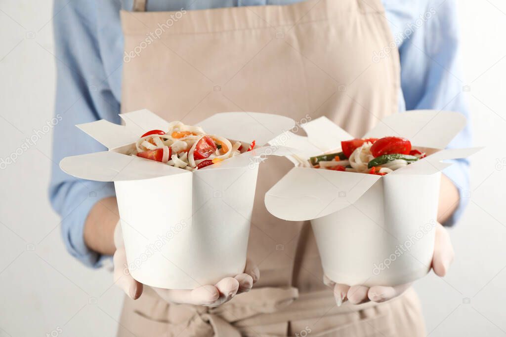 Chef holding boxes of vegetarian wok noodles on light background, closeup