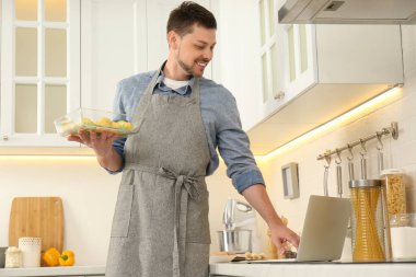 Adam mutfakta dizüstü bilgisayarla yemek pişirirken yemek yapıyor.