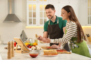 Mutfaktaki tabletten yemek kursunu izlerken birlikte pizza yapan mutlu çift.