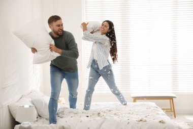 Mutlu genç çift yatak odasında yastık savaşı yapıyor.