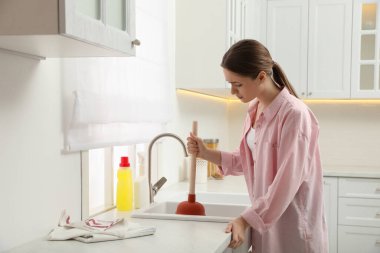 Genç bir kadın lavabo giderini açmak için lavabo pompası kullanıyor.