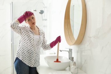 Banyodaki lavaboyu açmak için lavabo pompası kullanan yorgun genç bir kadın.