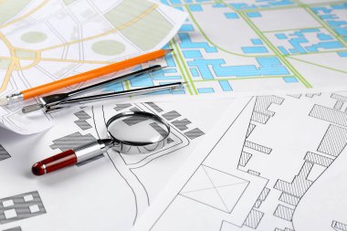Office stationery and magnifying glass on cadastral maps of territory with buildings clipart