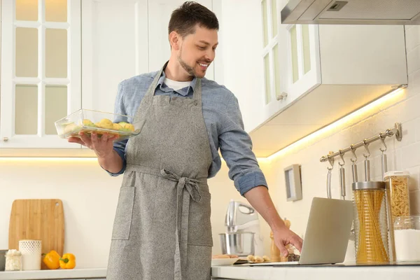 Adam mutfakta dizüstü bilgisayarla yemek pişirirken yemek yapıyor.