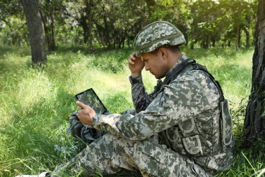 Ormanda ağaçların yanında tablet kullanan sırt çantalı asker.