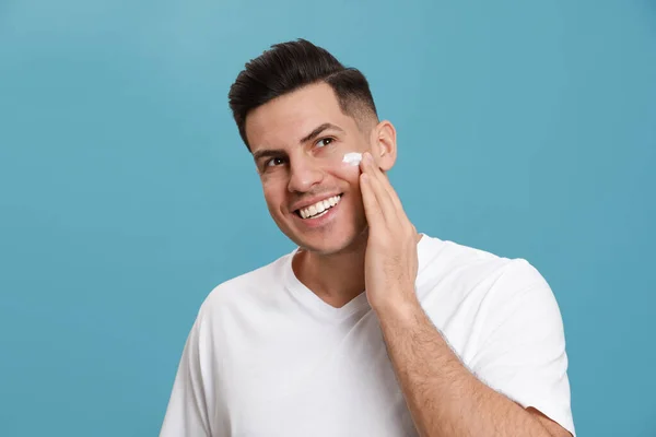 Feliz Homem Bonito Aplicando Creme Facial Contra Fundo Turquesa — Fotografia de Stock