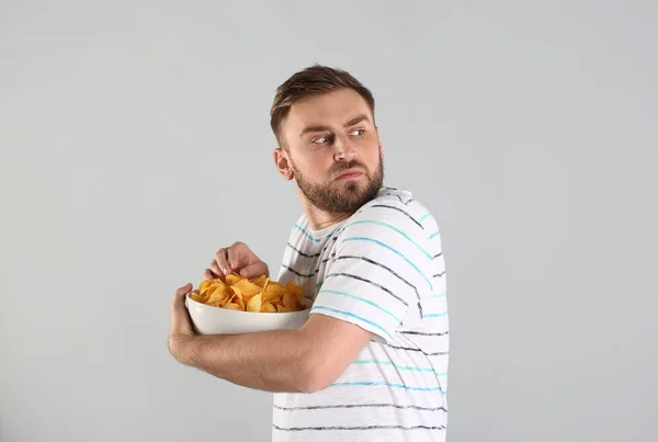 Greedy Young Man Hiding Bowl Chips Light Grey Background — Stock Photo, Image