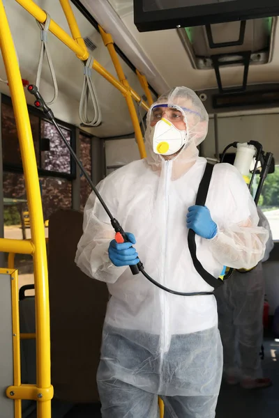 Public transport sanitation. Worker in protective suit disinfecting bus salon