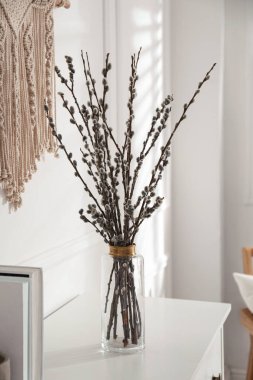 Glass vase with pussy willow tree branches on white table indoors