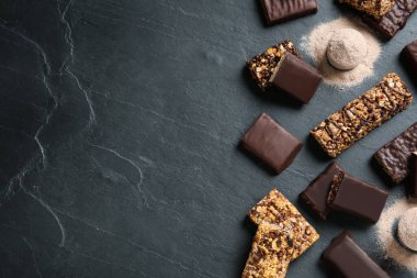 Farklı lezzetli enerji çubukları ve siyah masa üzerinde protein tozu, düz. Metin için boşluk