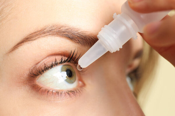 Young woman using eye drops on light background, closeup