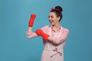 Açık mavi arka planda lastik eldiven giyen ev hanımı.