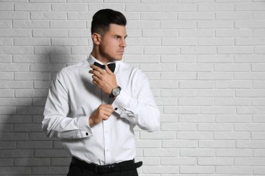 Beyaz tuğla duvarın yanında kol düğmesi takan yakışıklı bir adam. Metin için boşluk