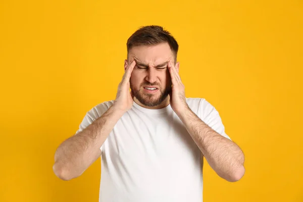 黄色の背景で片頭痛に苦しむ男 — ストック写真