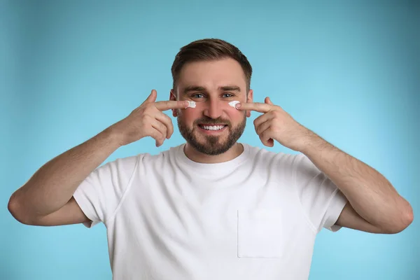 Happy Young Man Applying Facial Cream Light Blue Background — Stock Photo, Image