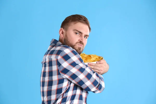 Greedy Young Man Hiding Bowl Chips Light Blue Background — Stock Photo, Image