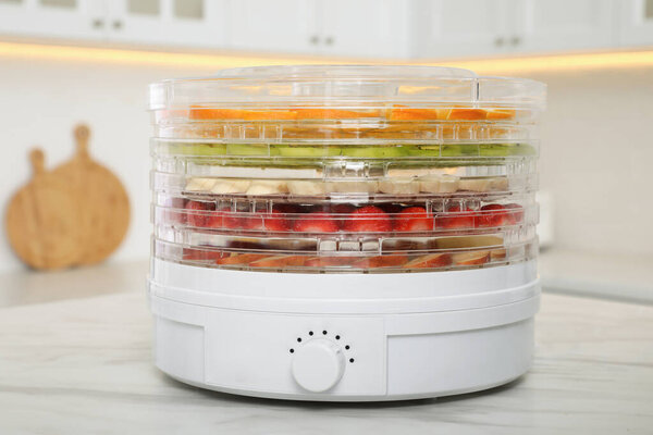 Дегидратор машина с различными фруктами и ягодами на белом мраморном столе на кухне