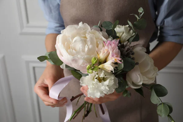 Florist creating beautiful bouquet at white wall, closeup