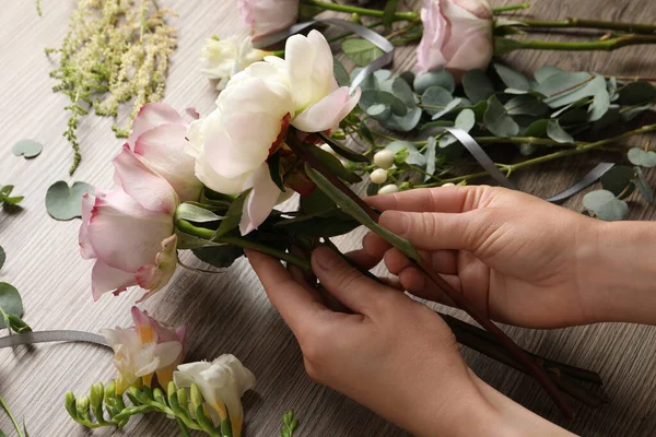 Florist creating beautiful bouquet at wooden table, closeup