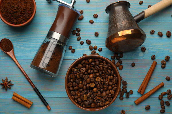 Manual coffee grinder with powder, beans and jezve on light blue wooden table, flat lay