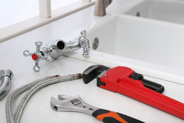 Parts of water tap and wrenches on white marble countertop in kitchen