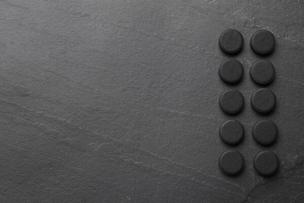 Activated charcoal pills and space for text on black table, flat lay. Potent sorbent