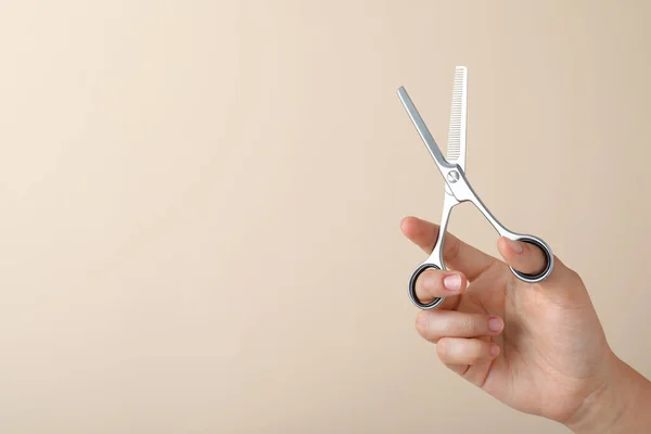 Hairdresser holding professional thinning scissors and space for text on beige background, closeup. Haircut tool