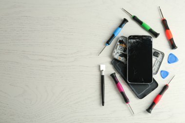 Beyaz ahşap arka planda hasarlı akıllı telefon ve tamir aletleri, düz konum. Metin için boşluk