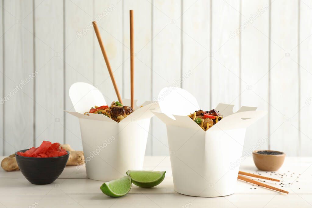 Boxes of wok noodles with vegetables, meat and chopsticks on white wooden table