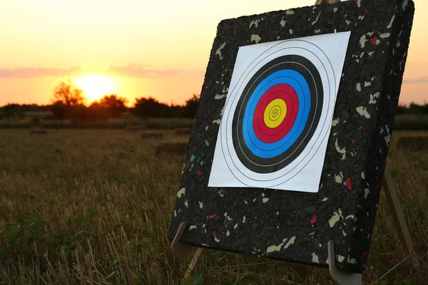 Tripod with archery target in field at sunset